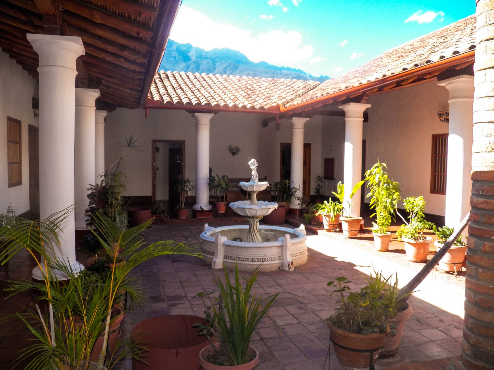 Patio central con la fuente blanca de dos platos, columnas y la sierra al fondo