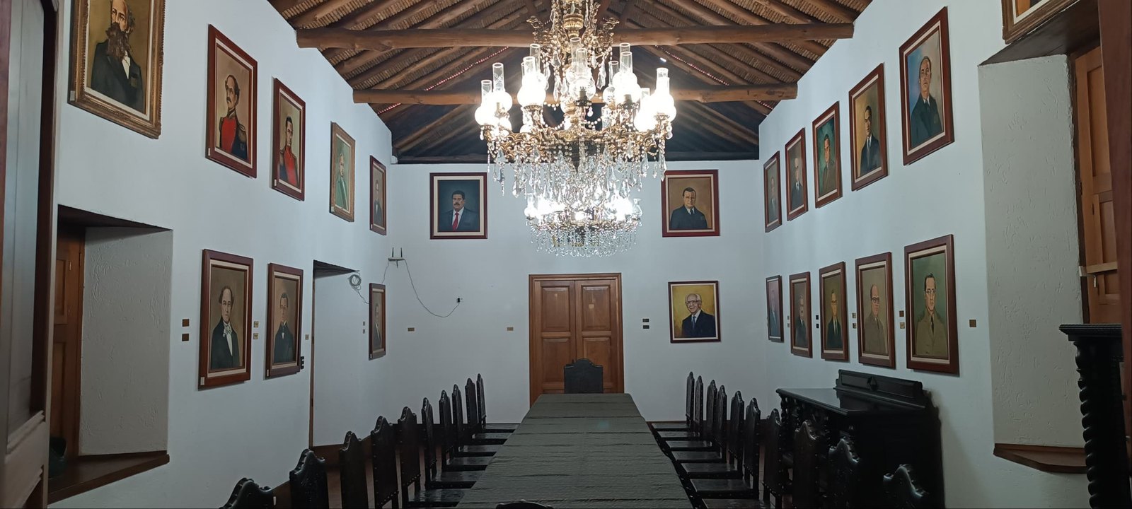 Salón alargado con la mesa de sesiones y su lámpara de araña